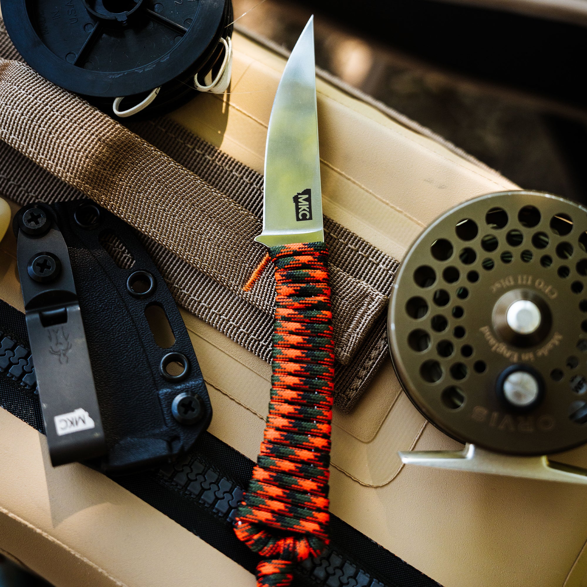ONX Hunt Mini-Speedgoat 2.0 knife with a paracord handle, surrounded by fishing gear and tactical accessories.