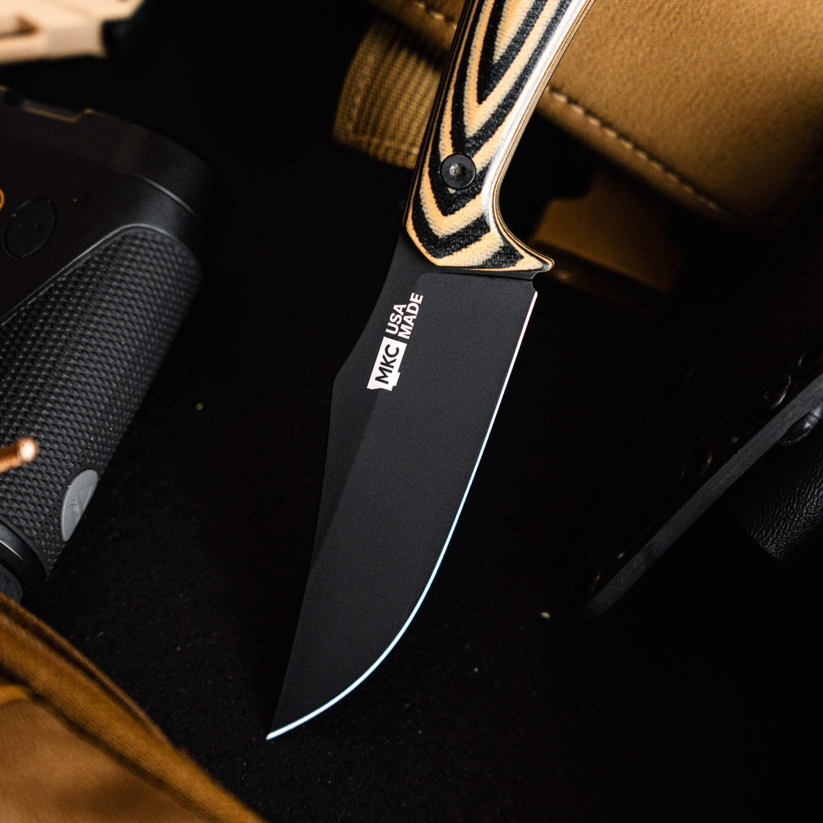 Triumph Pro knife with a tan and black handle, featuring a sleek black blade, resting on a textured surface.