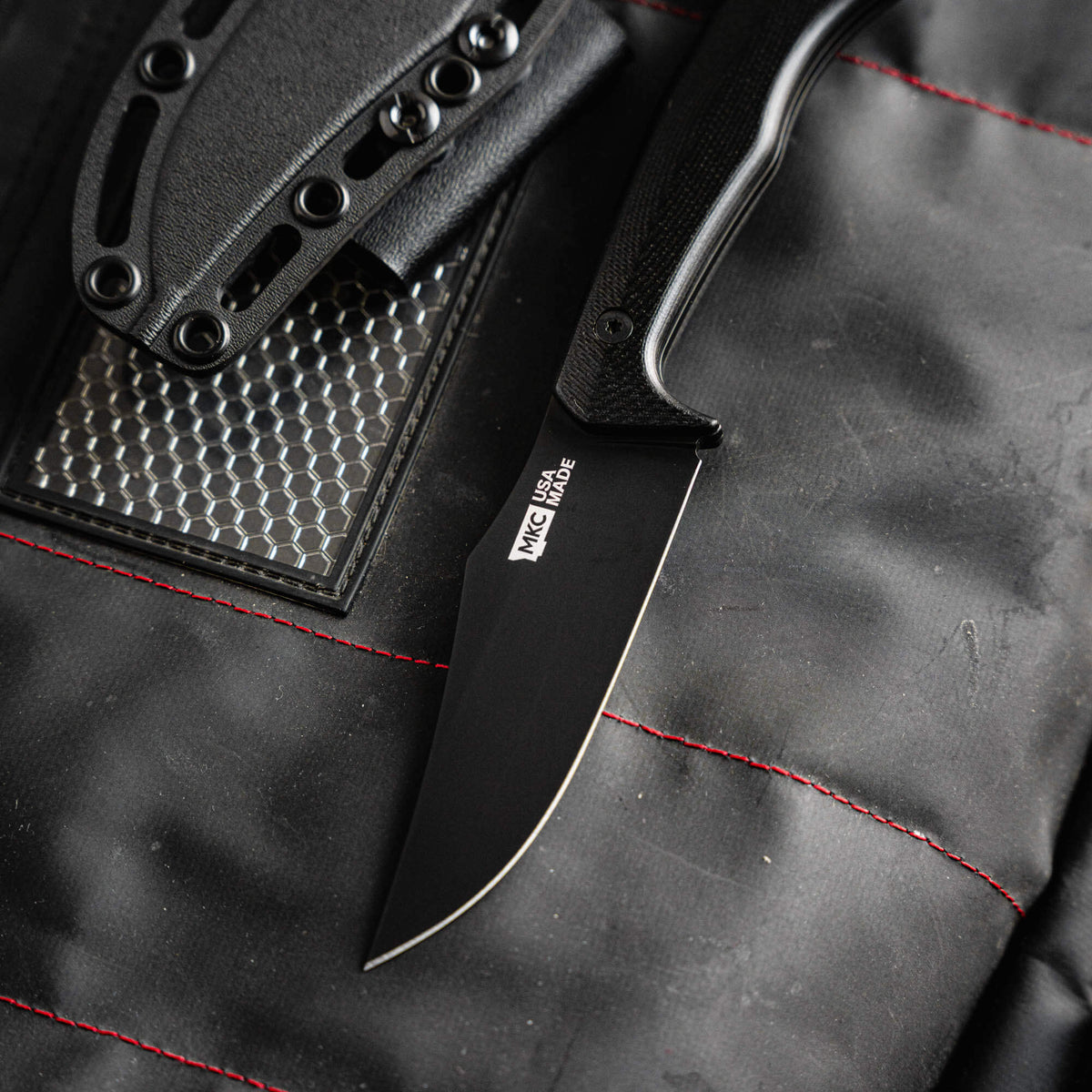 Black Triumph Pro knife with a sleek blade and textured handle, resting on a padded surface with gear.
