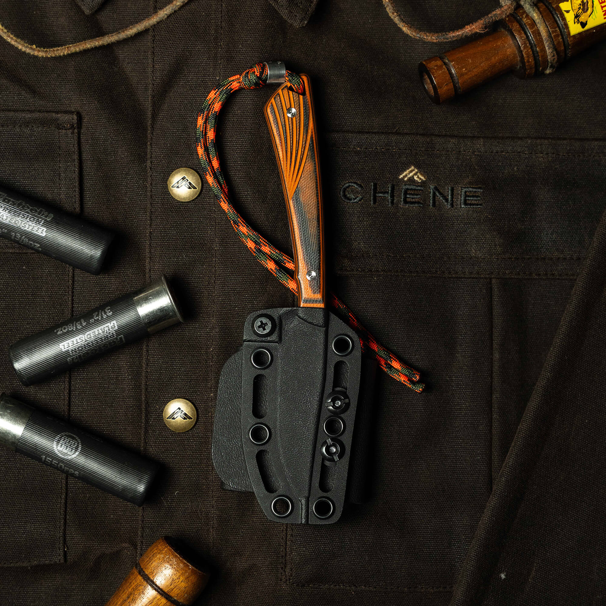 Montana Knife Company's CHÊNE Freezout knife displayed on a dark shirt with tools, showcasing its rugged design and craftsmanship.