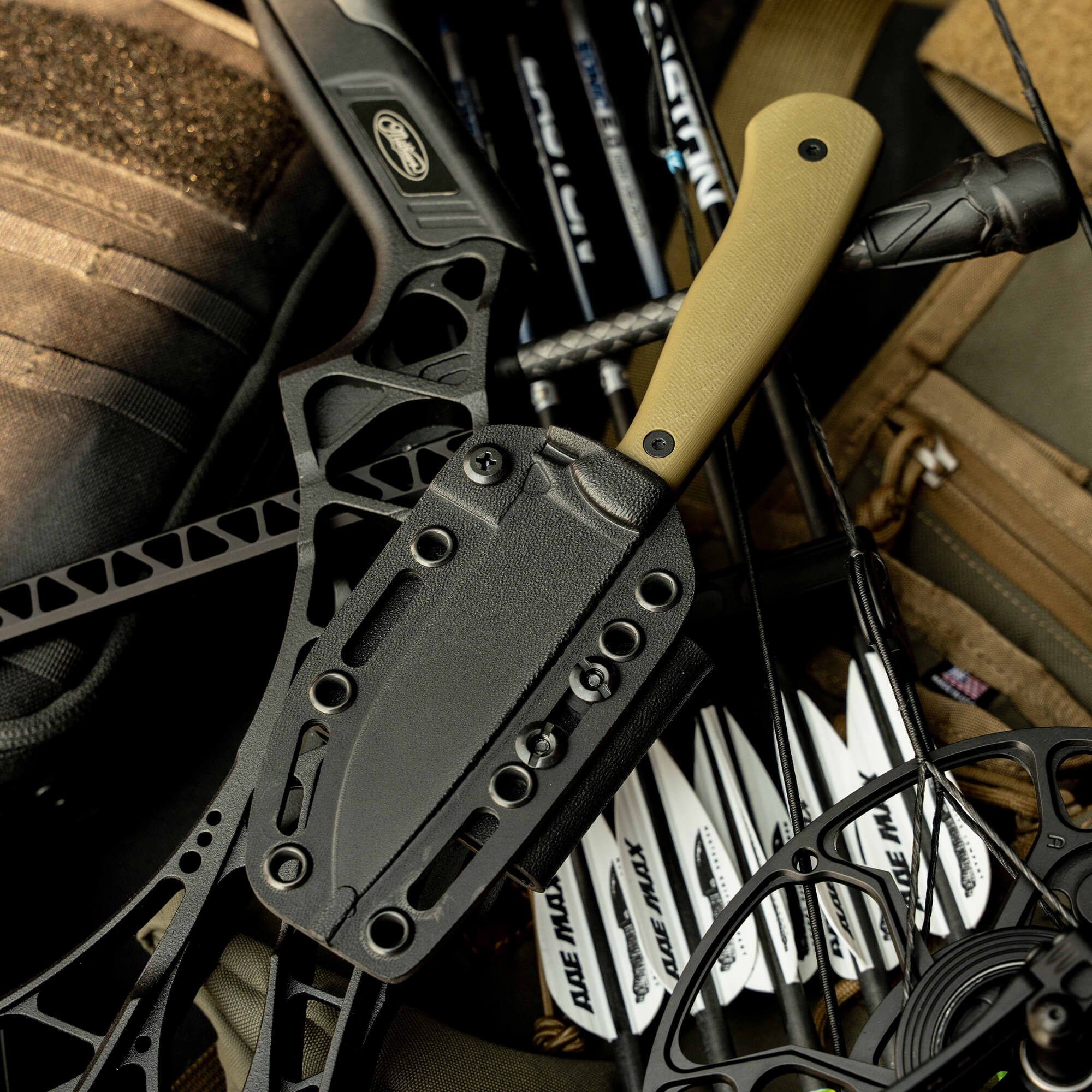 MKC Whitetail knife nestled among archery gear, featuring a sleek black blade and a durable tan handle.