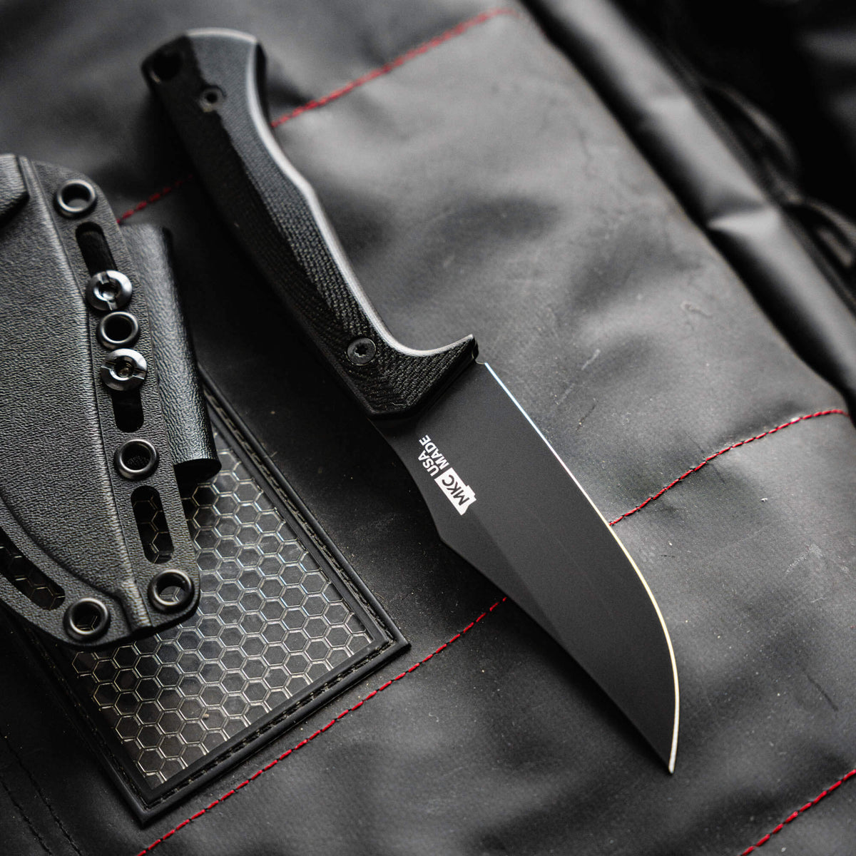 Triumph Pro Black knife with a sleek blade and textured handle, displayed on a black surface with red stitching.