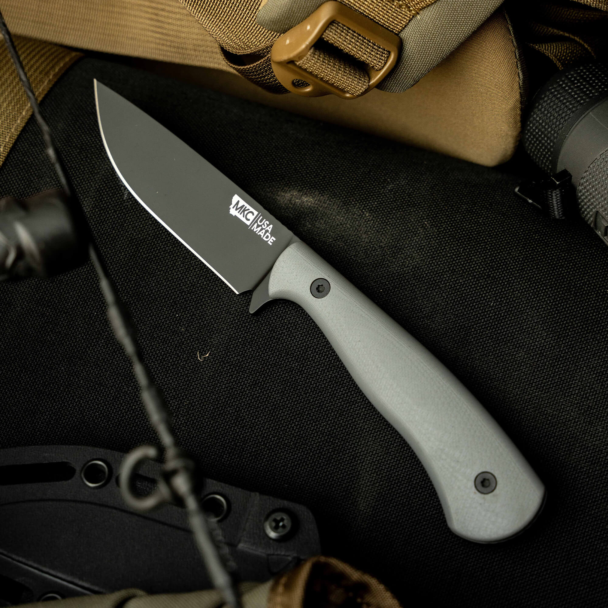 Mathews Archery MKC Whitetail knife with a gray handle, resting on tactical gear, ideal for hunting and outdoor use.