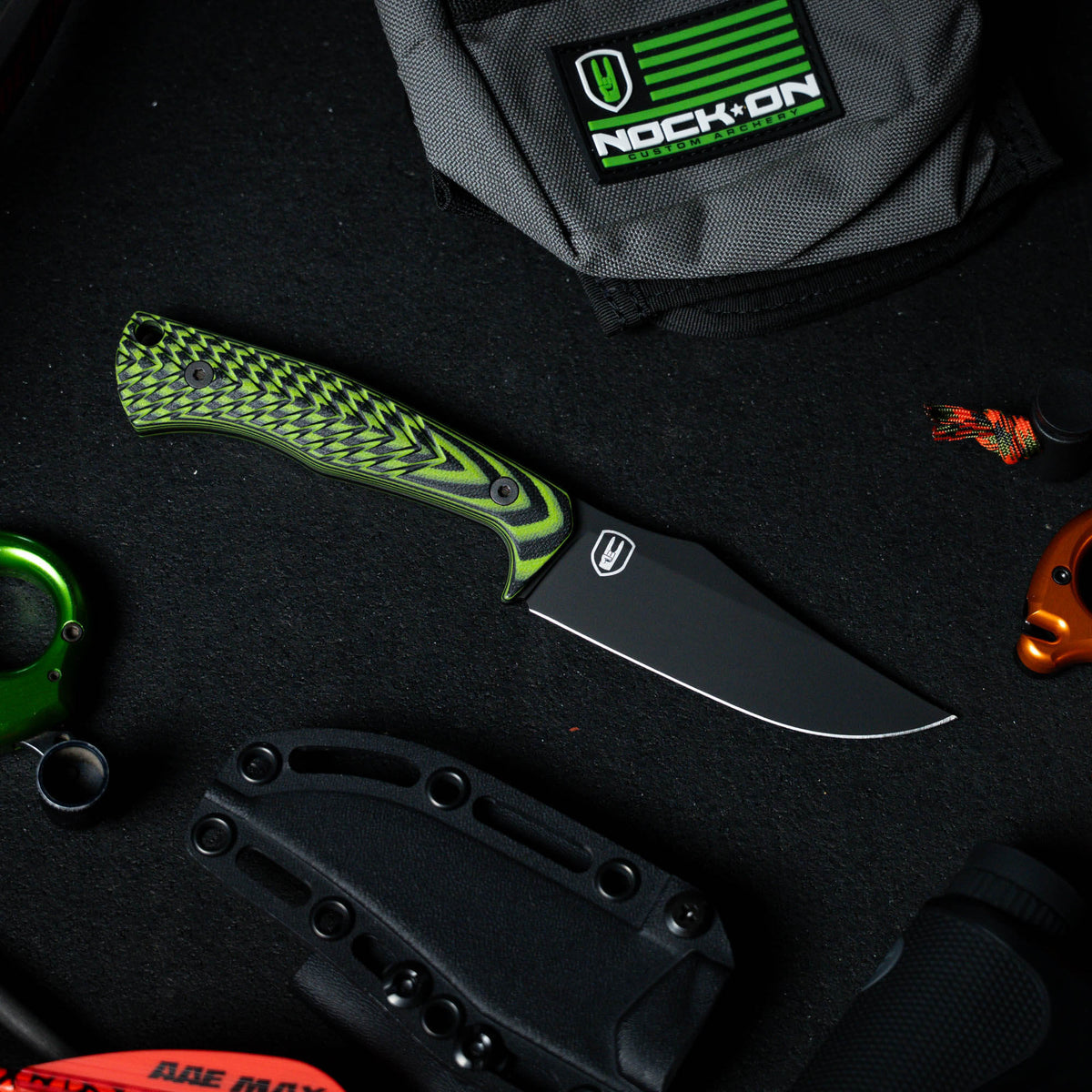 Triumph Pro knife in neon green and black with a textured handle, featuring a black blade, surrounded by gear.