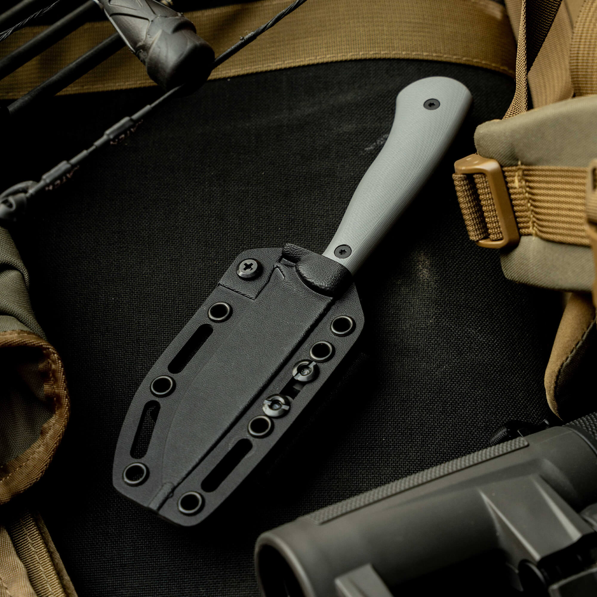 Mathews Archery MKC Whitetail knife with a sleek black sheath, resting on tactical gear and equipment.