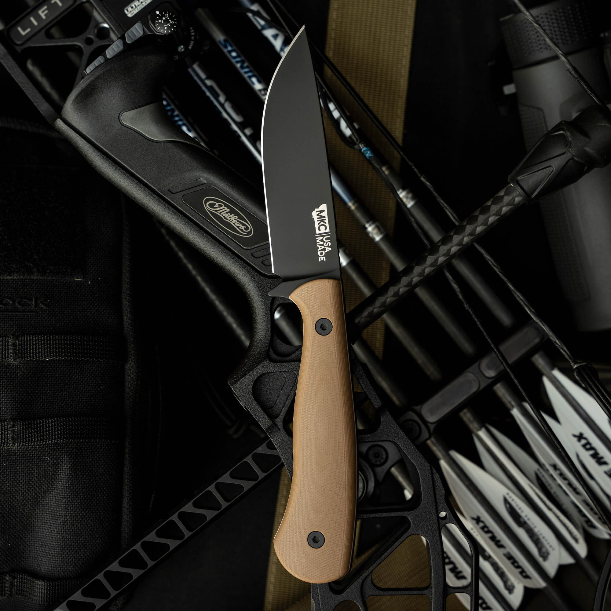 Mathews Archery MKC Whitetail knife with a sleek black blade and tan handle, positioned among archery gear.