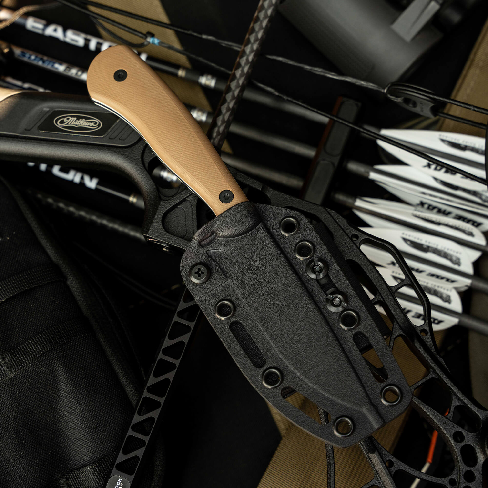 Mathews Archery MKC Whitetail knife with a tan handle, resting among arrows and gear, showcasing its tactical design.