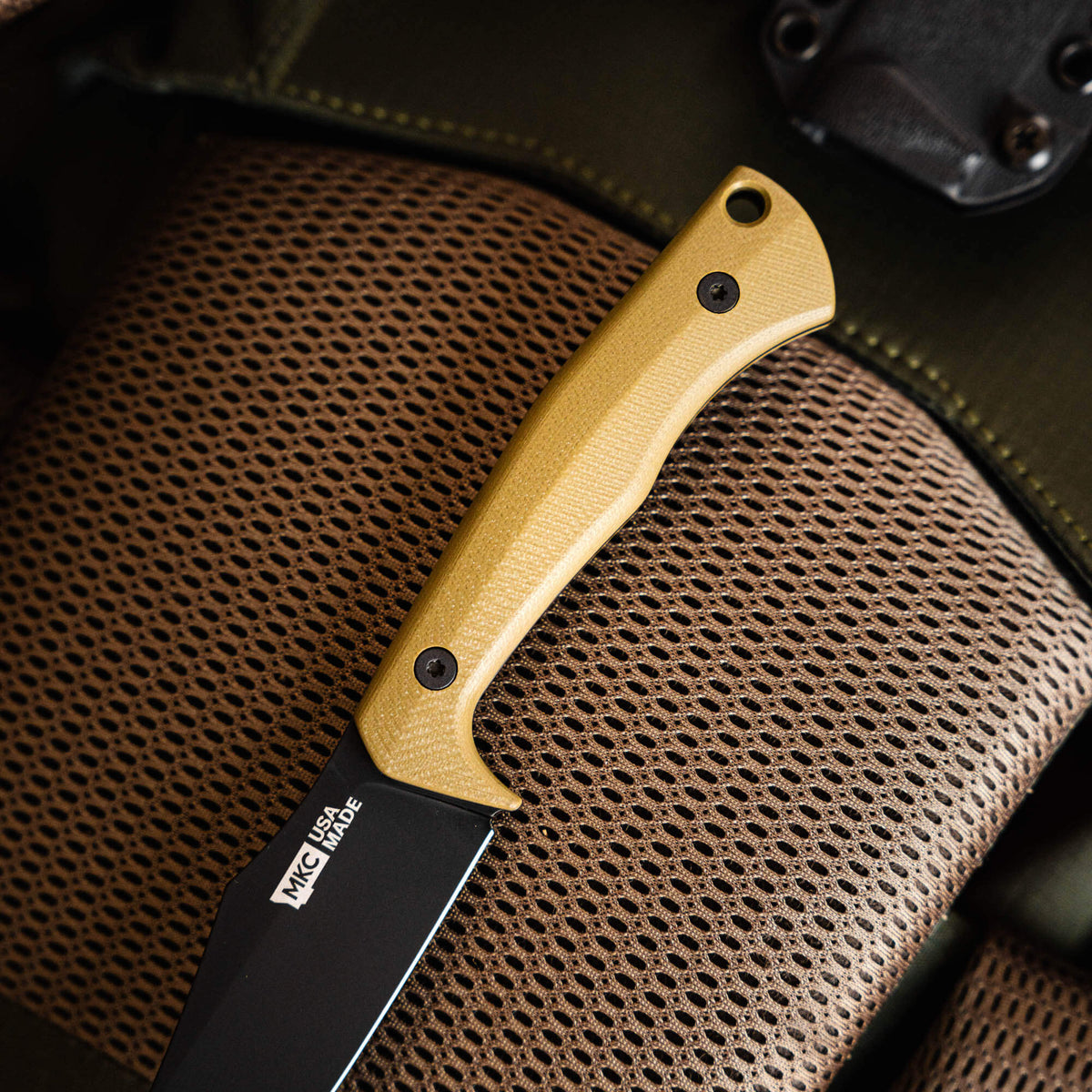Olive handle of the TRIUMPH PRO knife resting on a textured surface, showcasing its rugged design and craftsmanship.