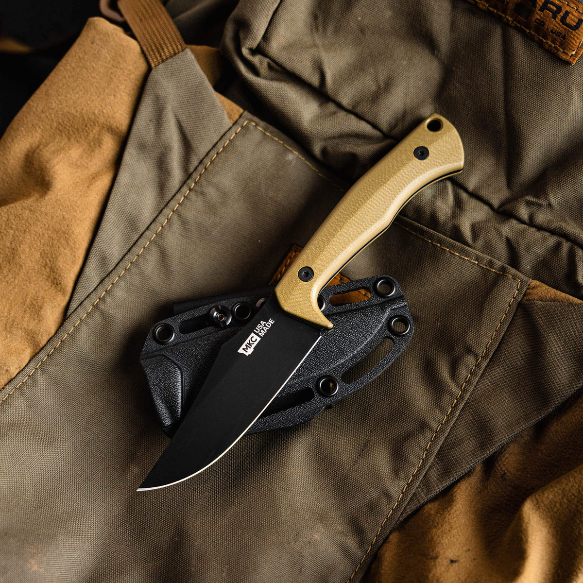 Olive handle Triumph Pro knife resting on a tactical pouch, showcasing its sleek blade and durable sheath.