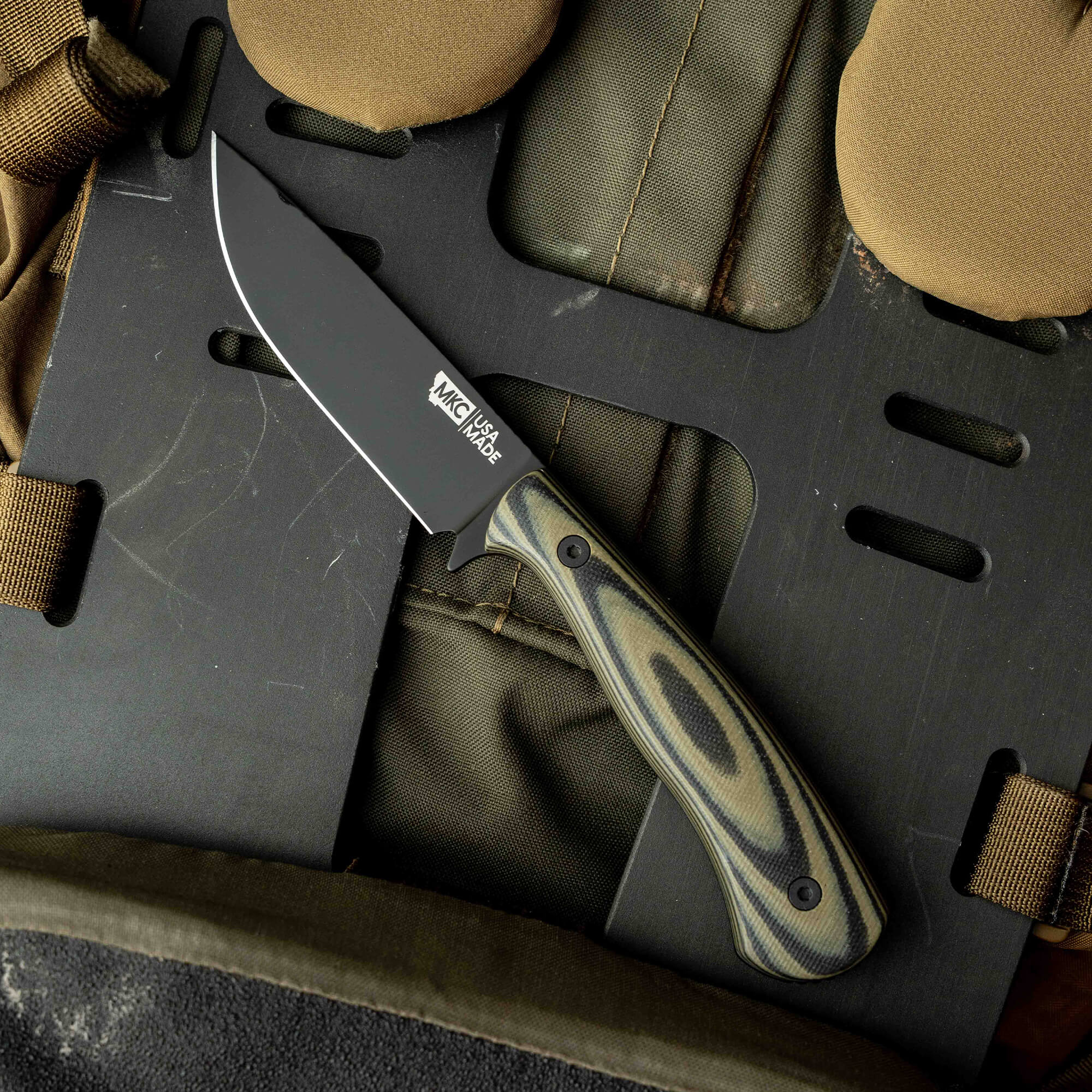 Mathews Archery MKC Whitetail knife with a black blade and patterned handle, resting on tactical gear background.