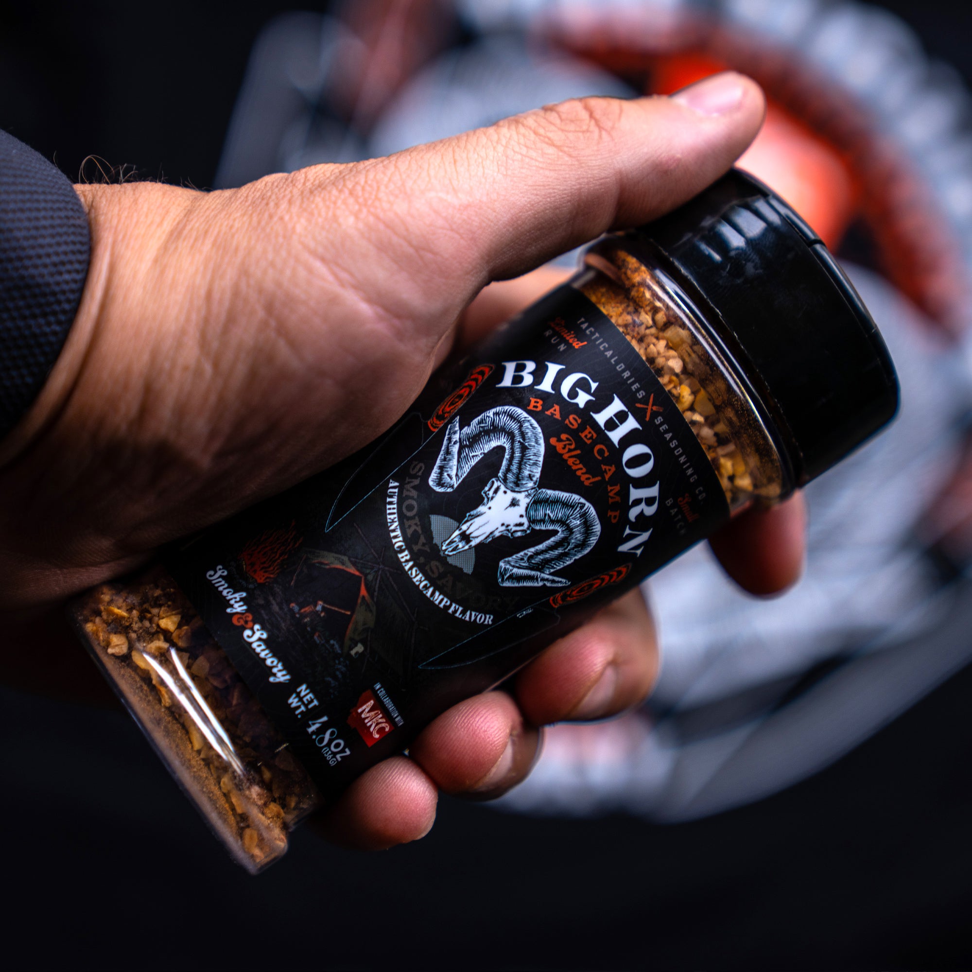 Close-up view of a person's hand holding a bottle of BIGHORN Basecamp Seasoning, showcasing the label with a ram's head logo and visible spices inside the jar.