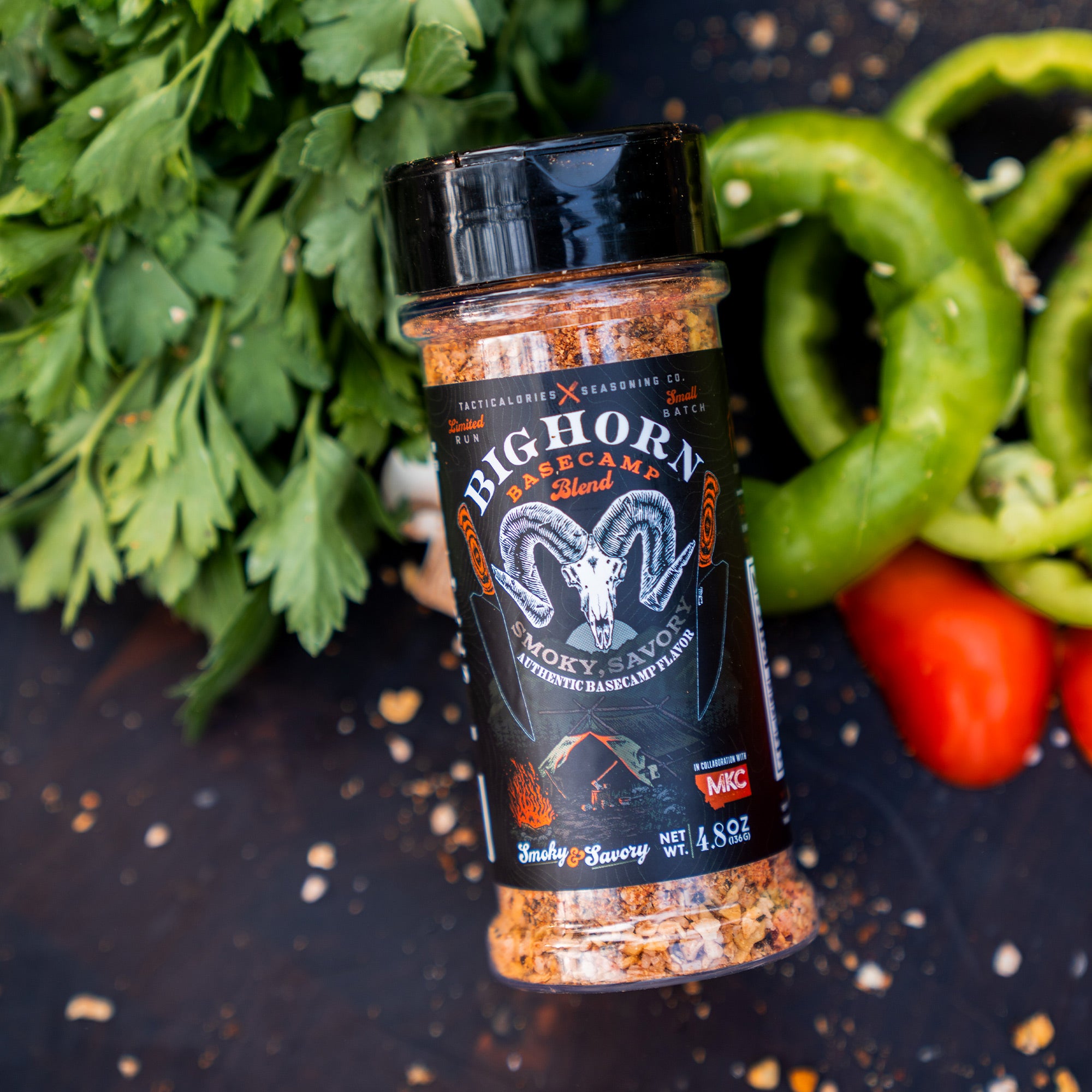 A bottle of Bighorn Basecamp seasoning blend, featuring a smoky and savory flavor, displayed with fresh green bell peppers and parsley in the background.